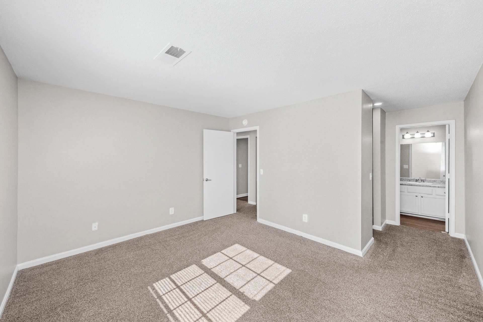 Empty carpeted bedroom with gray walls, open closet doors, and an adjoining bathroom visible.