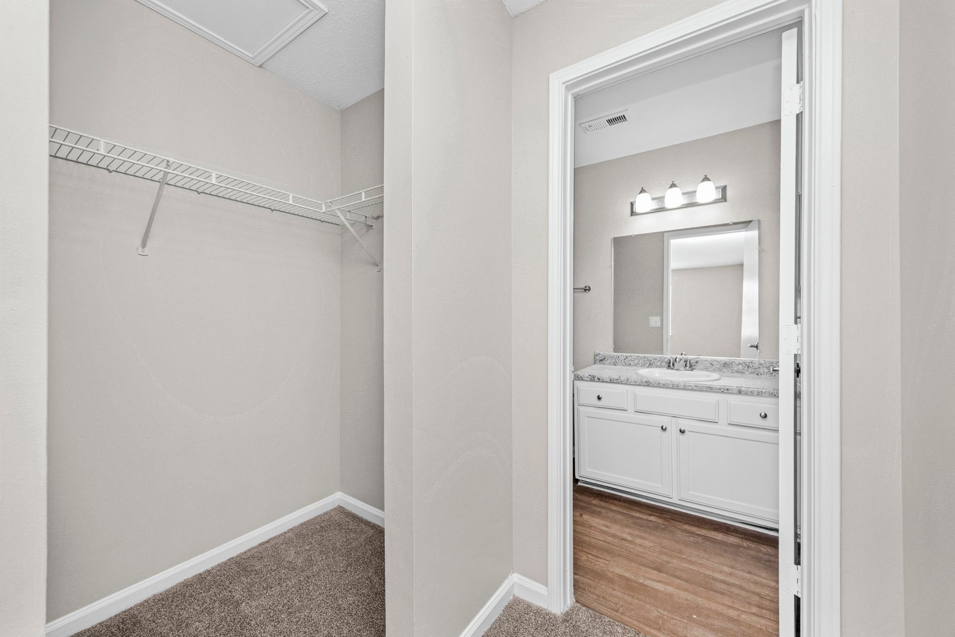 Empty walk-in closet beside a bathroom with white walls, wire shelf, and beige carpet/flooring.