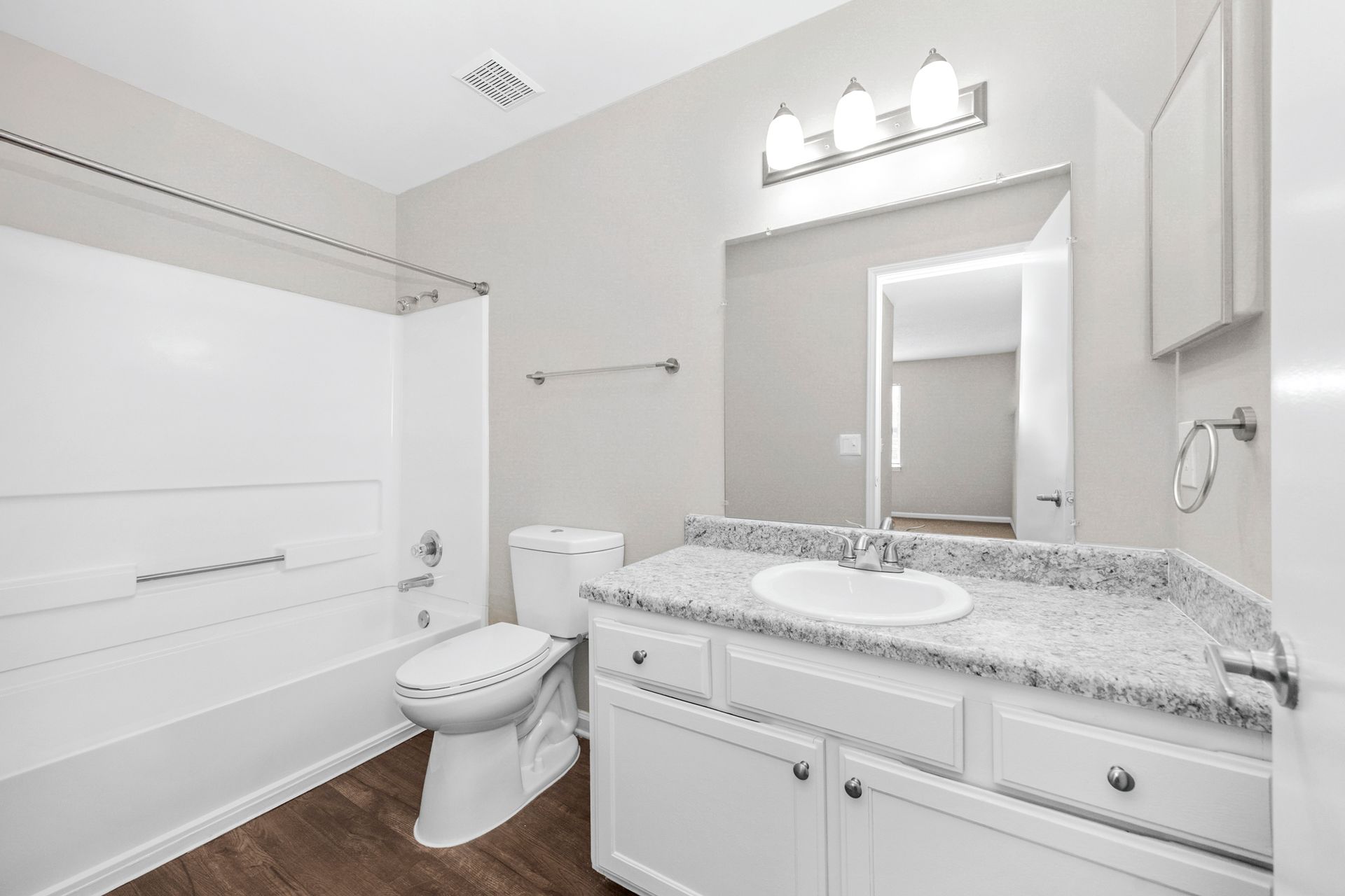 Bright white bathroom with tub-shower, toilet, vanity, and large mirror