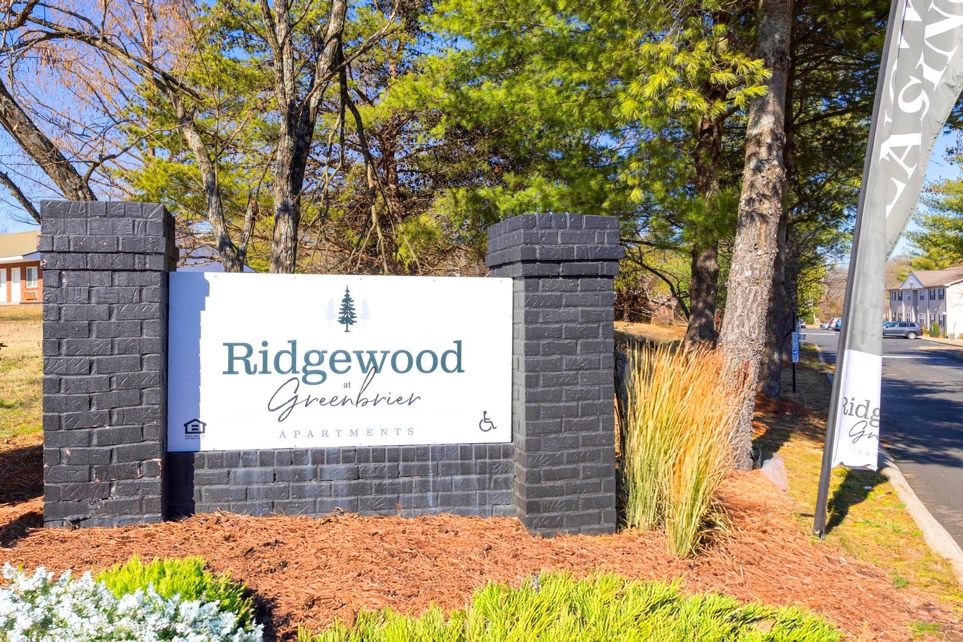 Ridgewood Green apartment entrance sign by brick pillars and trees on a sunny day