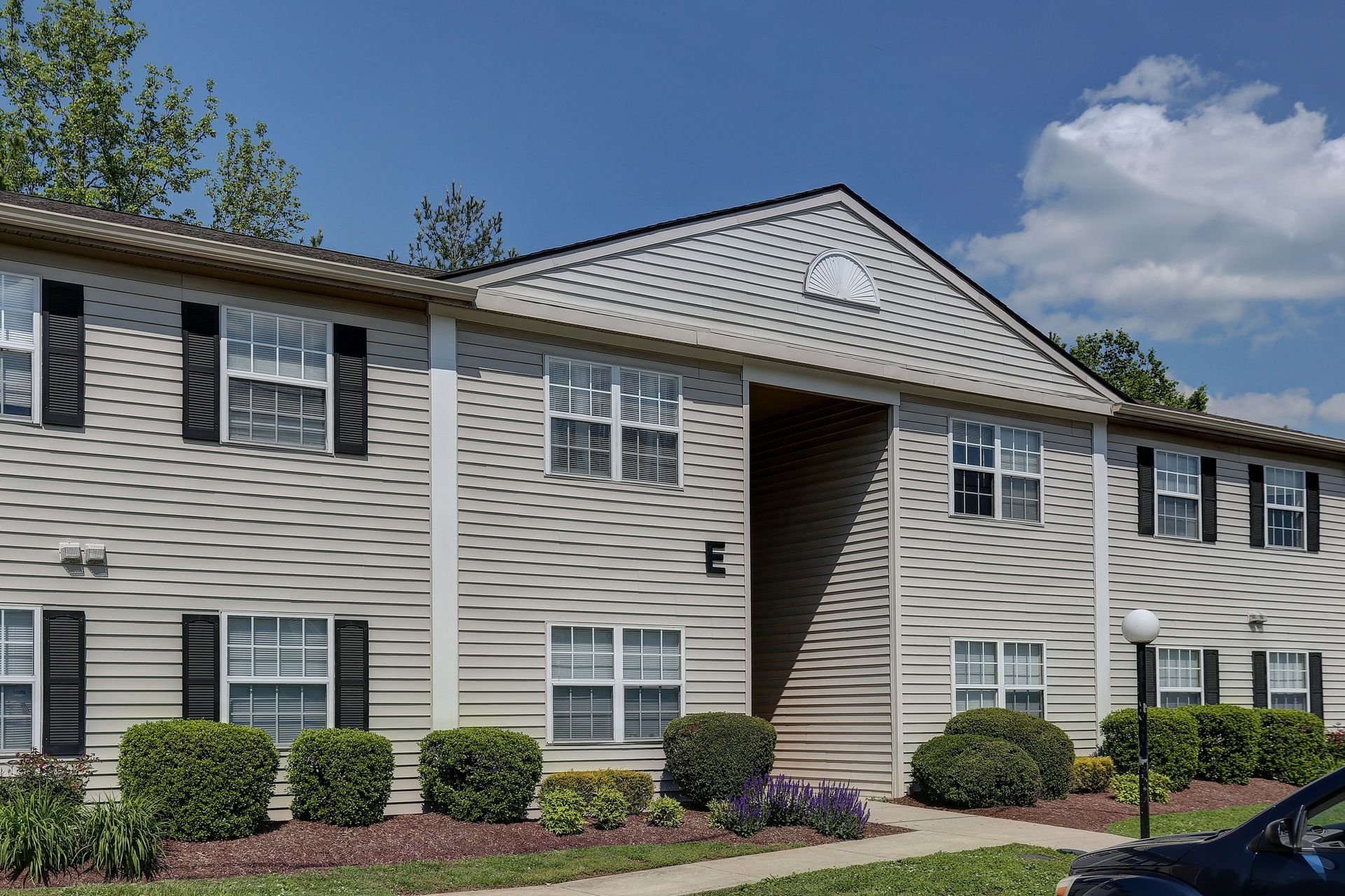 Apartment building exterior with beige siding, white trim, shrubs, and blue sky