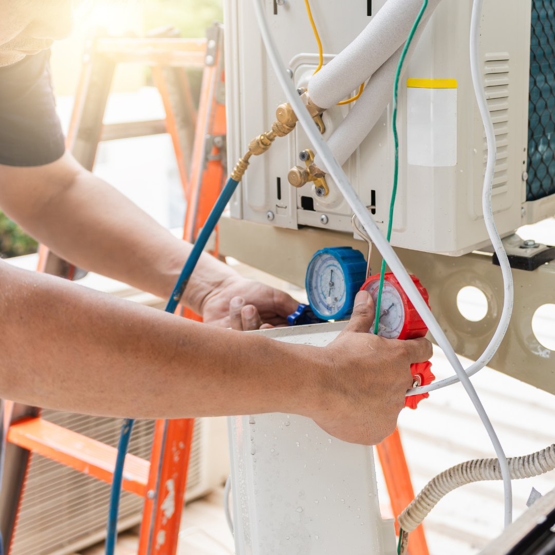 Person working on an air conditioning unit using gauges. Orange ladder in background.