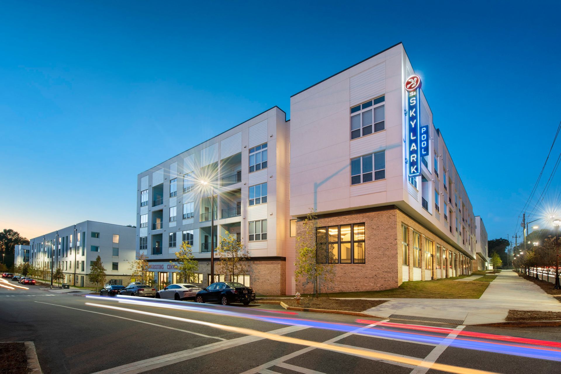Modern apartment building at dusk with lit windows and streetlights on a city corner