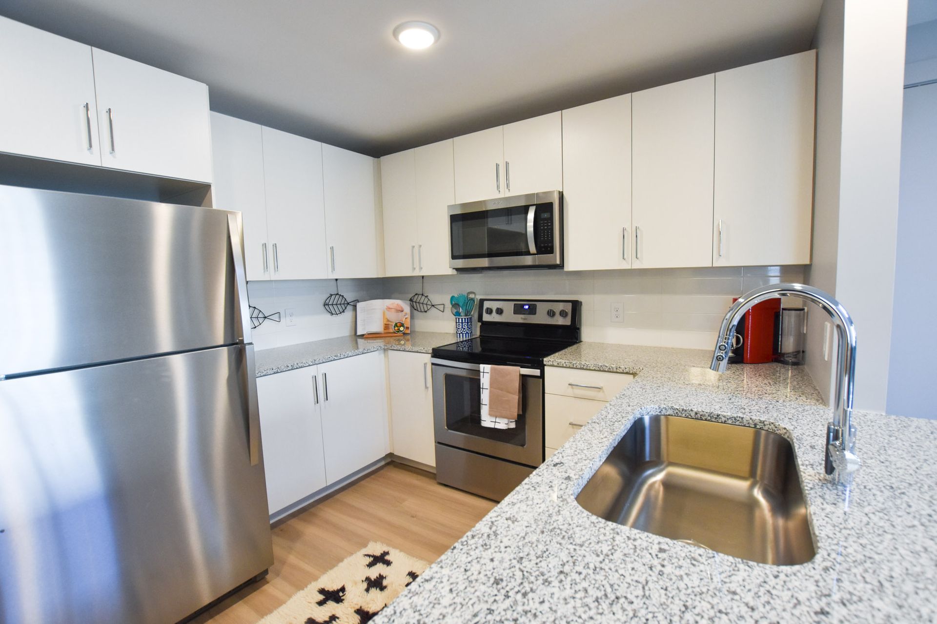 Modern kitchen with stainless steel appliances, white cabinets, speckled countertops, and a double sink