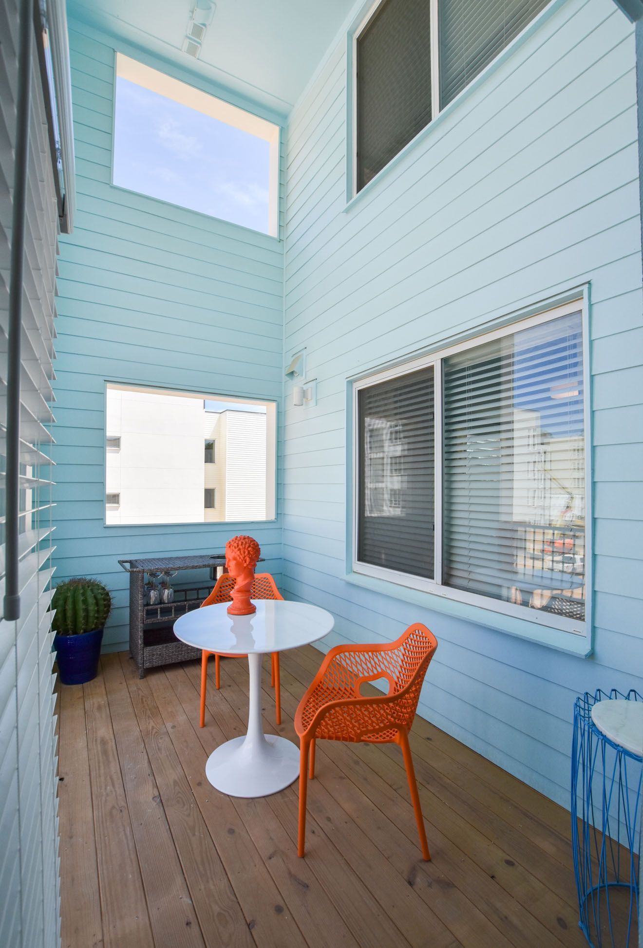 Light blue courtyard with orange chairs, white table, and potted plants beneath tall windows