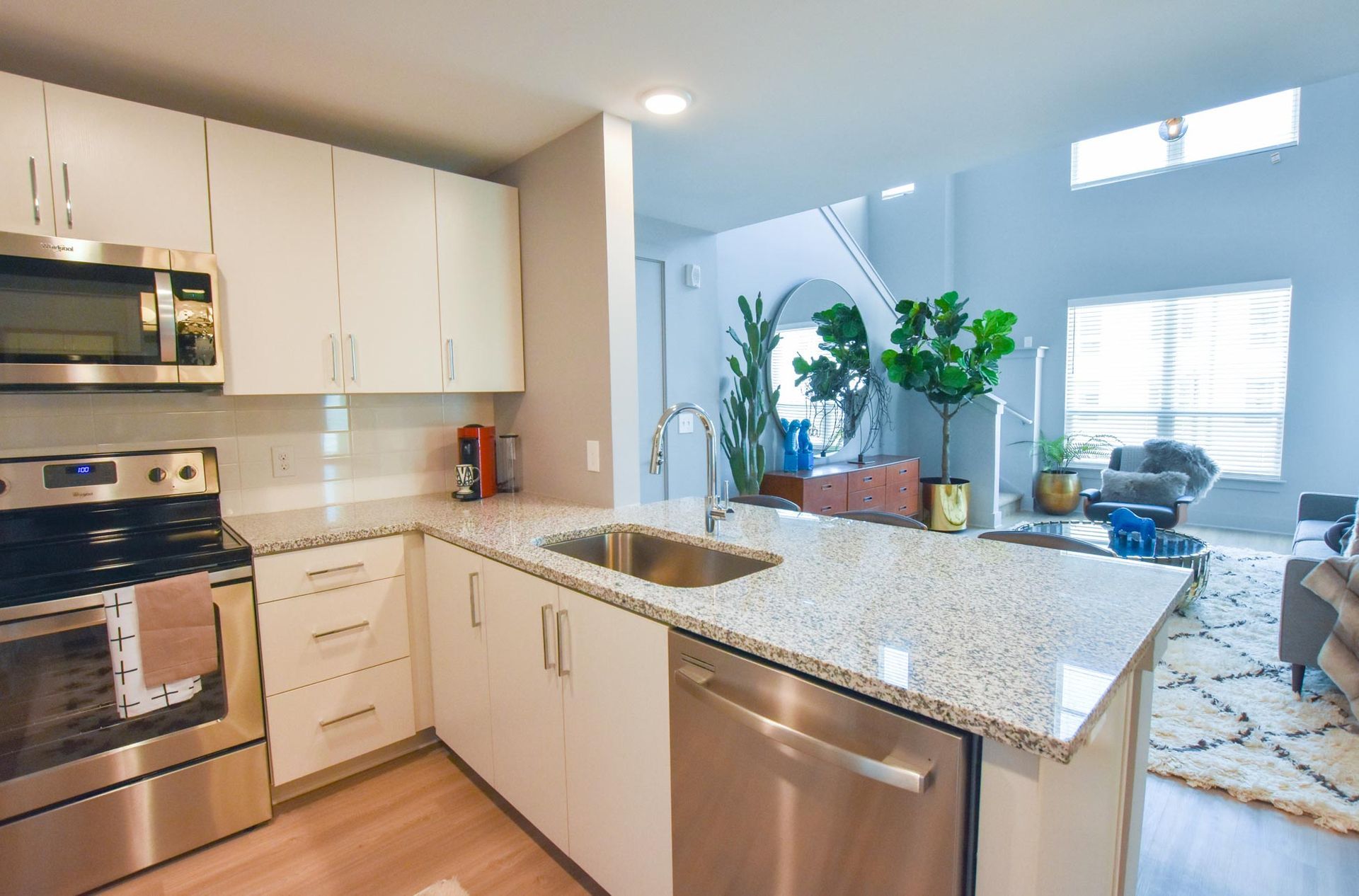 Bright modern kitchen with white cabinets, granite island, stainless appliances, and living room beyond
