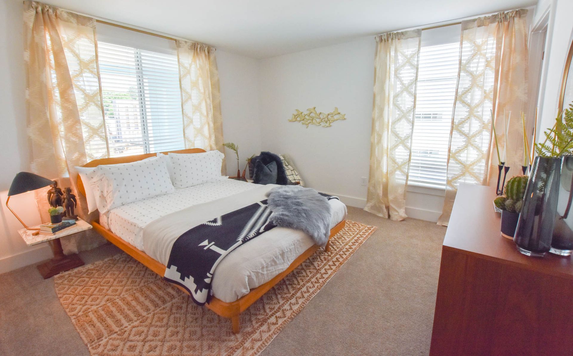 Bright bedroom with a made bed, patterned curtains, and a dresser by the window.