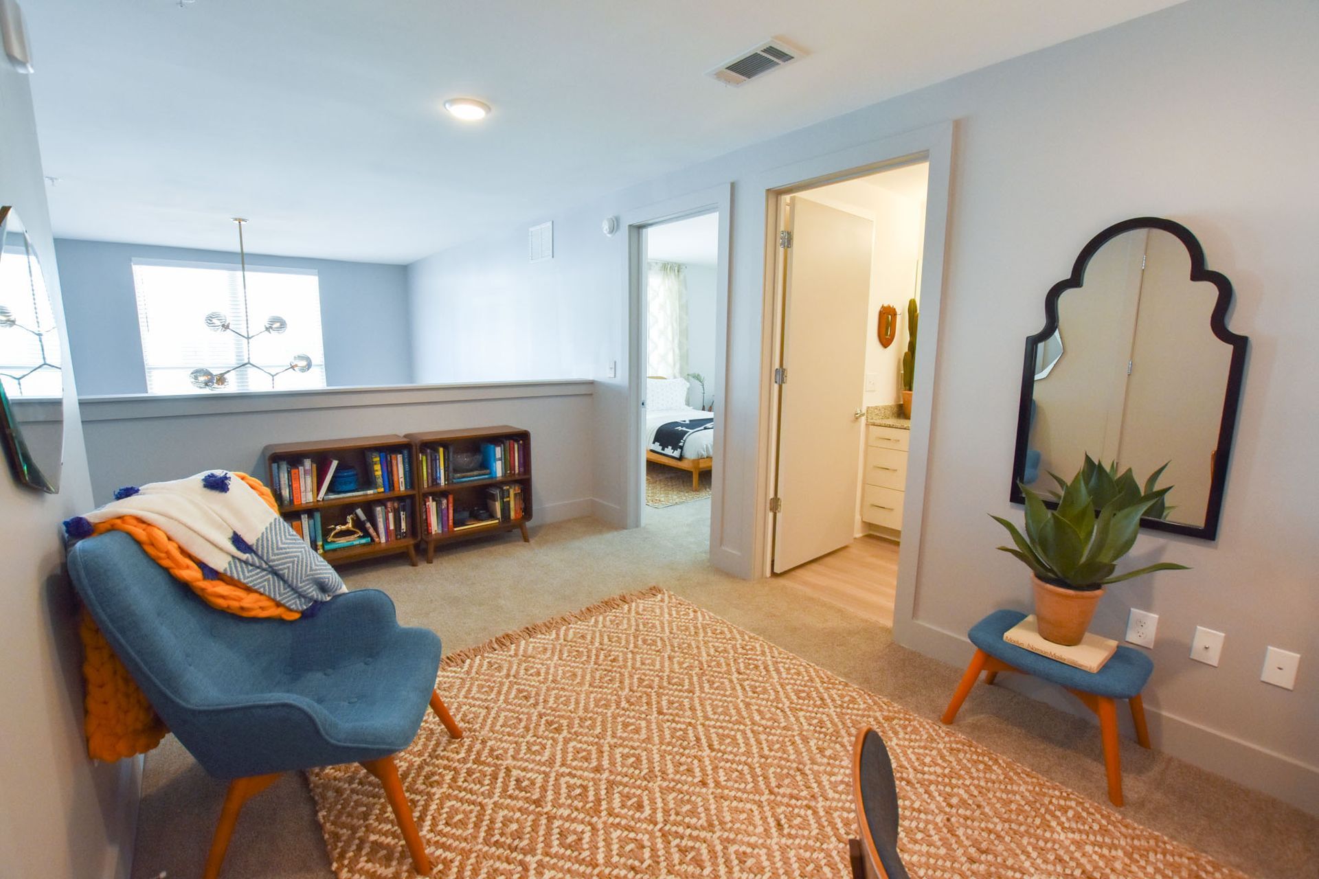 Cozy living room with blue sofa, patterned rug, bookshelf, mirror, and open doorway to a lit hall