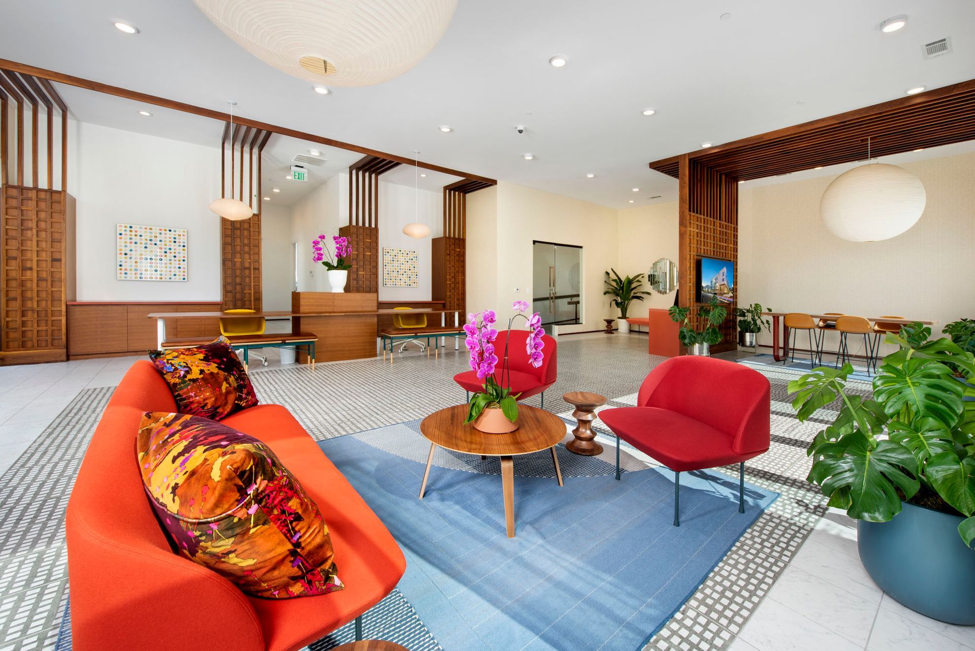 Modern hotel lobby with red chairs, wooden tables, and patterned carpet under a large ceiling light