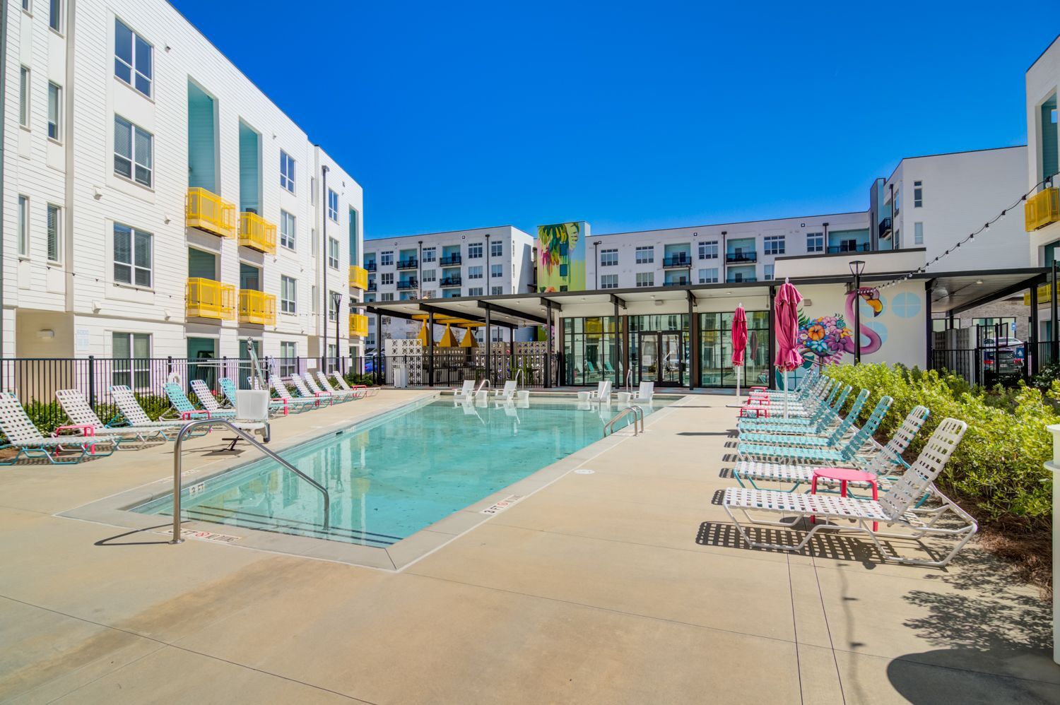 Modern apartment courtyard with a turquoise pool, lounge chairs, and colorful wall art