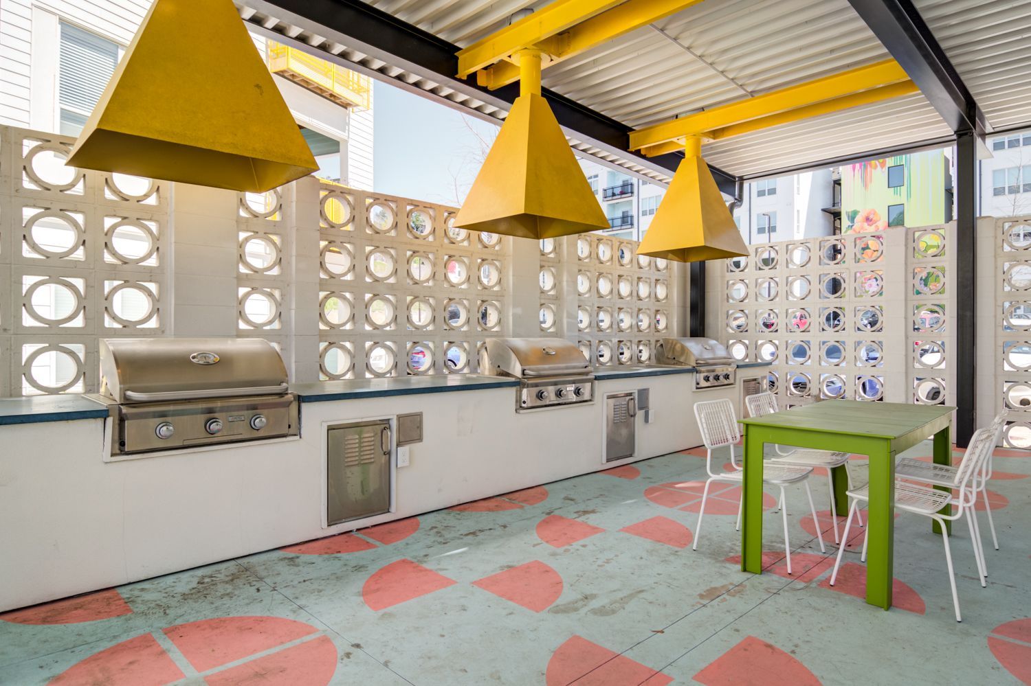 Covered outdoor patio with yellow pendant lights, grill, sink, and colorful patterned floor tiles