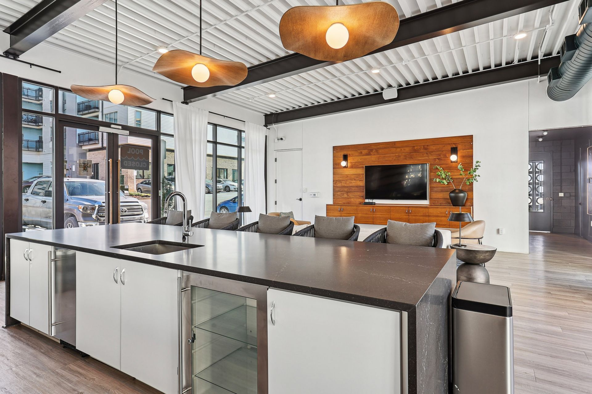 Modern open office kitchen and lounge with large island, pendant lights, exposed ceiling, and brick TV wall