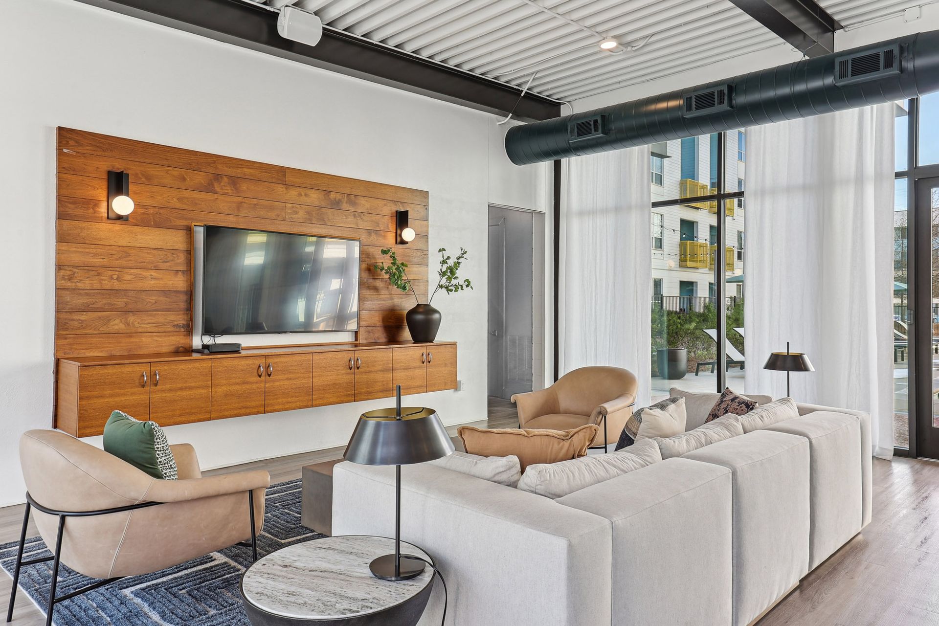 Modern living room with white sofas, tan chairs, wood TV wall, and large windows
