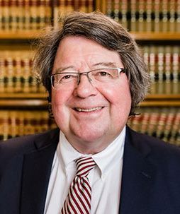 A man in a suit and tie is smiling in front of a bookshelf.