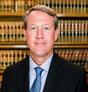 A man in a suit and tie is standing in front of a bookshelf.