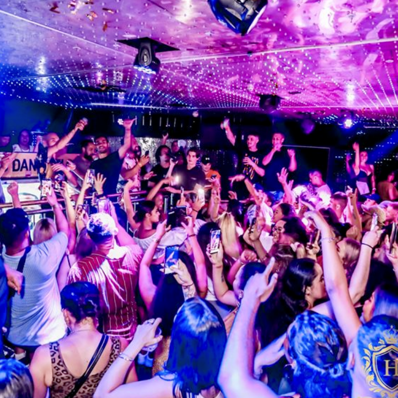 A crowd of people are dancing in a club with their hands in the air.