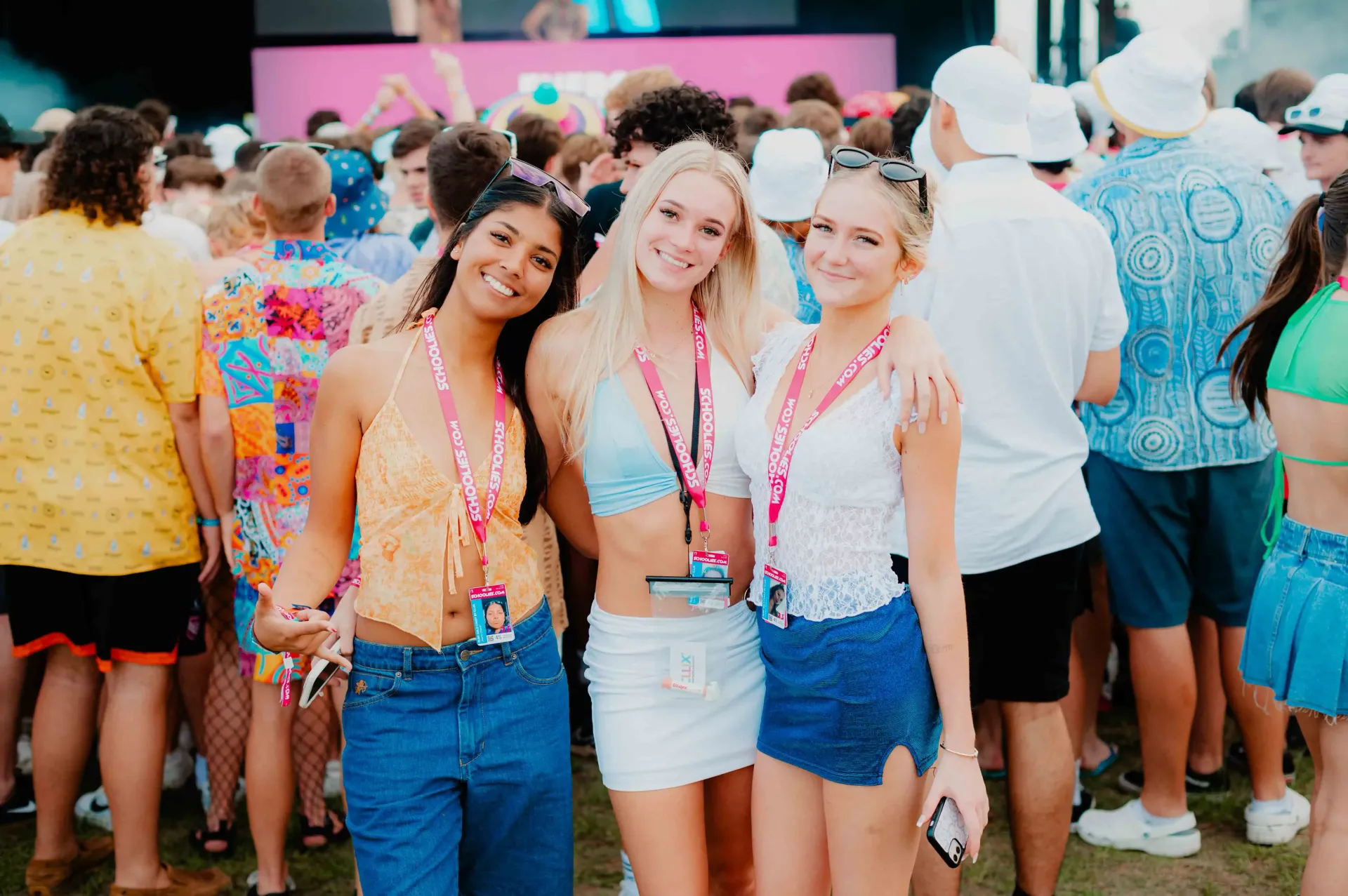 Three women are posing for a picture in front of a crowd of people at a music festival.