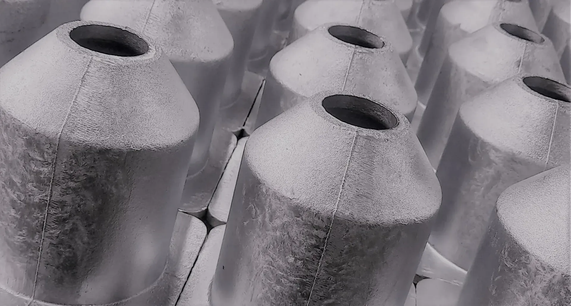 File di strutture argentate a forma di cono con sommità aperta, probabilmente di design industriale o architettonico.