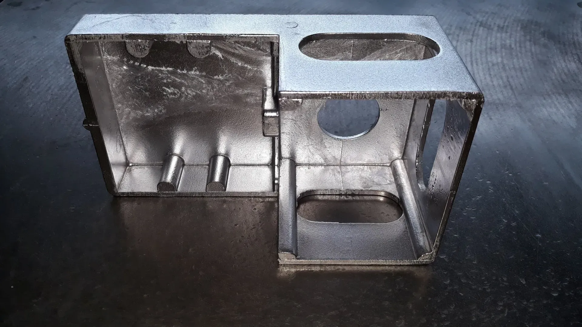 Scatola metallica con aperture rettangolari e circolari, lato incernierato, due montanti metallici.