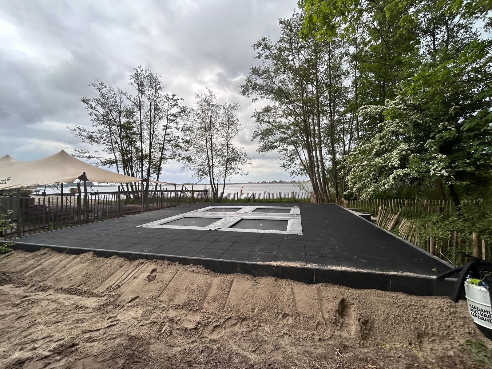 Trampolineplatform met uitzicht op het water, omgeven door bomen en een bewolkte hemel.