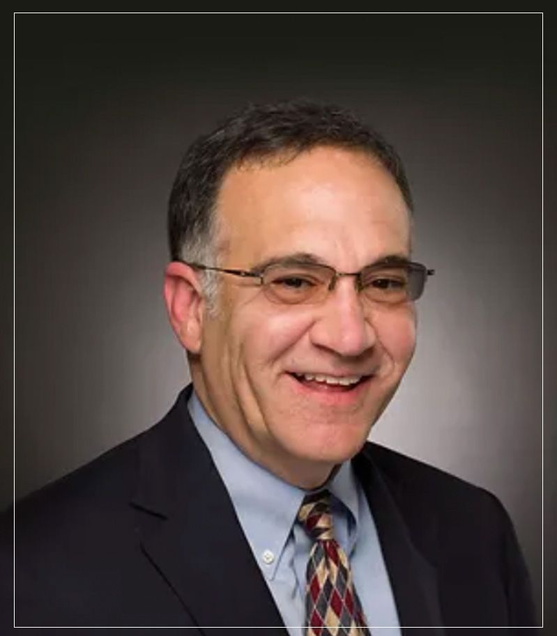 Smiling man in glasses and suit against a dark gradient background