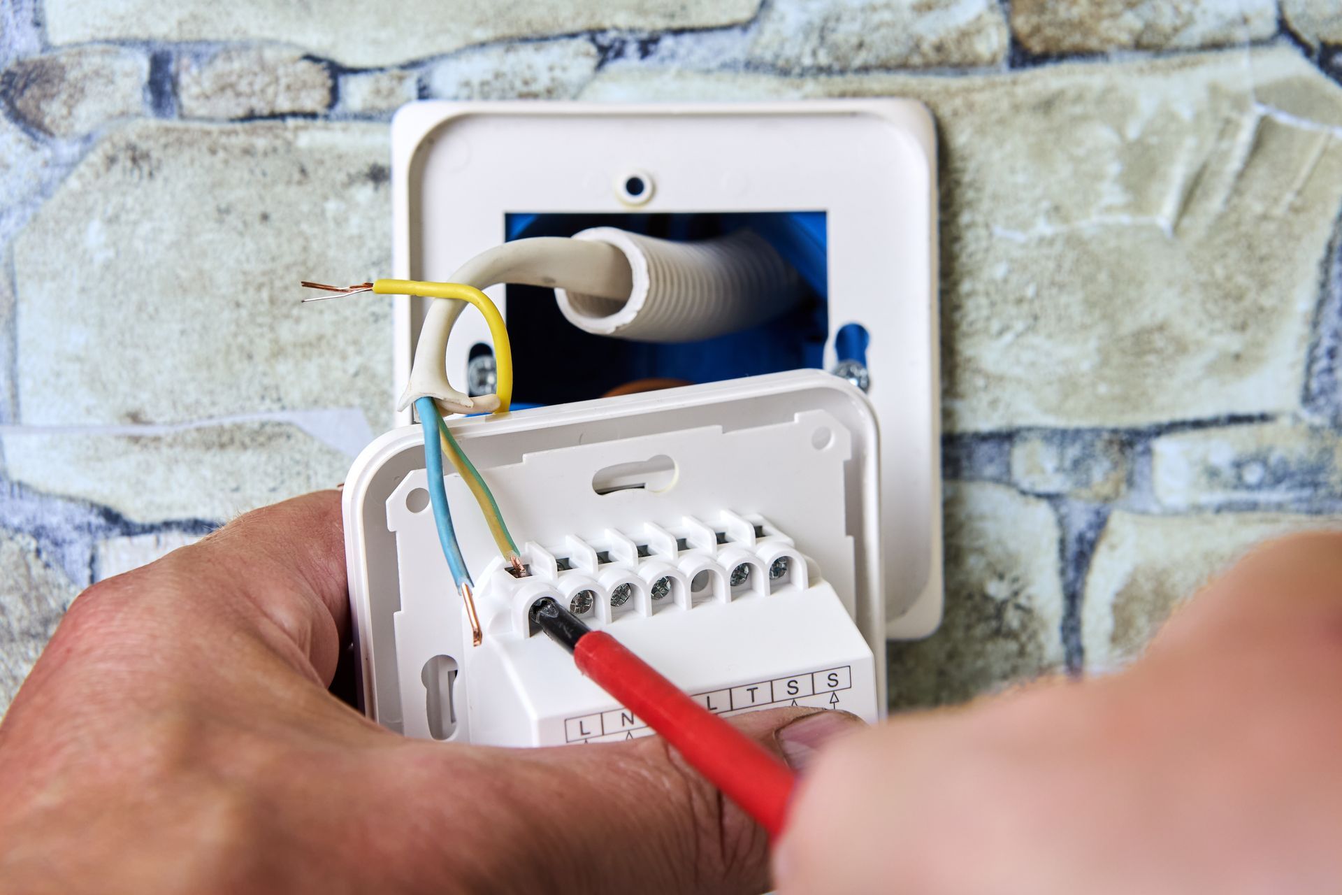 Hand connecting wires to an outdoor electrical junction box on a stone wall