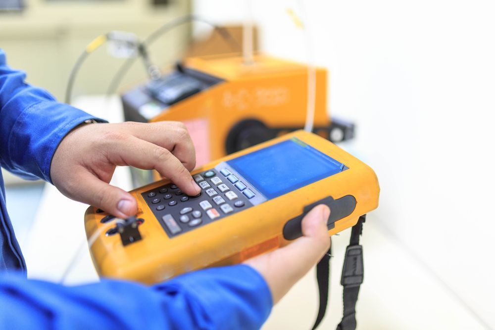 Hands holding an orange handheld instrument with a keypad and screen in a lab setting