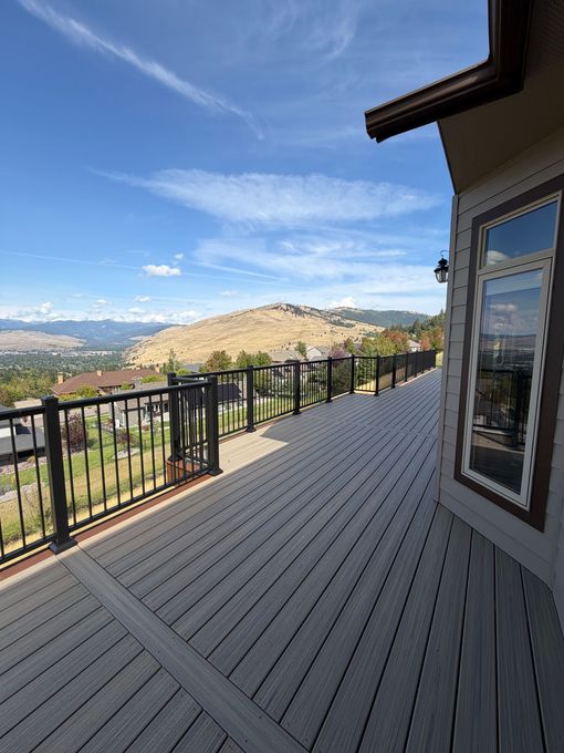 Wooden deck with glass railing overlooks a city and fall foliage.