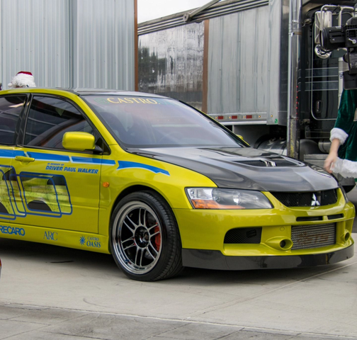 Yellow Mitsubishi sedan with racing decals parked beside a truck in an industrial lot