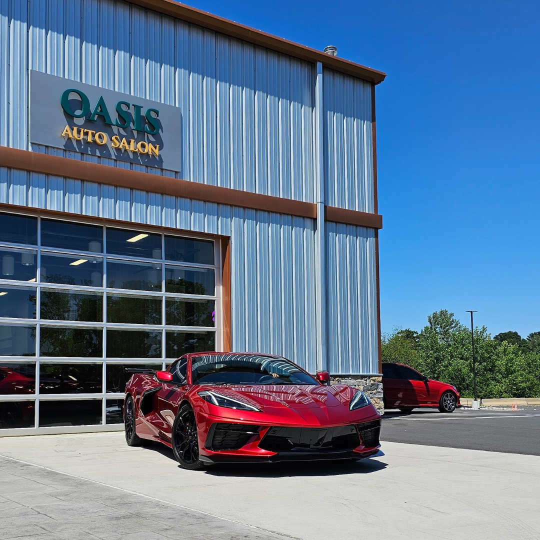 A shiny red Corvette parked in front of an Oasis Auto Salon building under a clear blue sky.