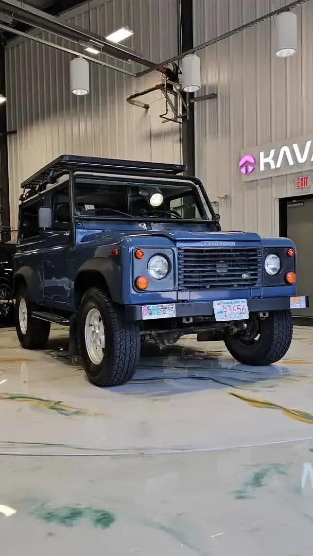 Blue off-road SUV parked indoors in a garage or showroom with a KAVA sign on the wall