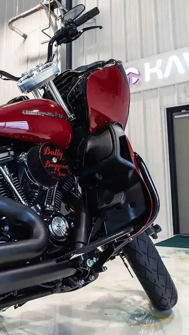 Close-up, low-angle view of a maroon Harley-Davidson motorcycle parked indoors, highlighting the front fairing and engine.