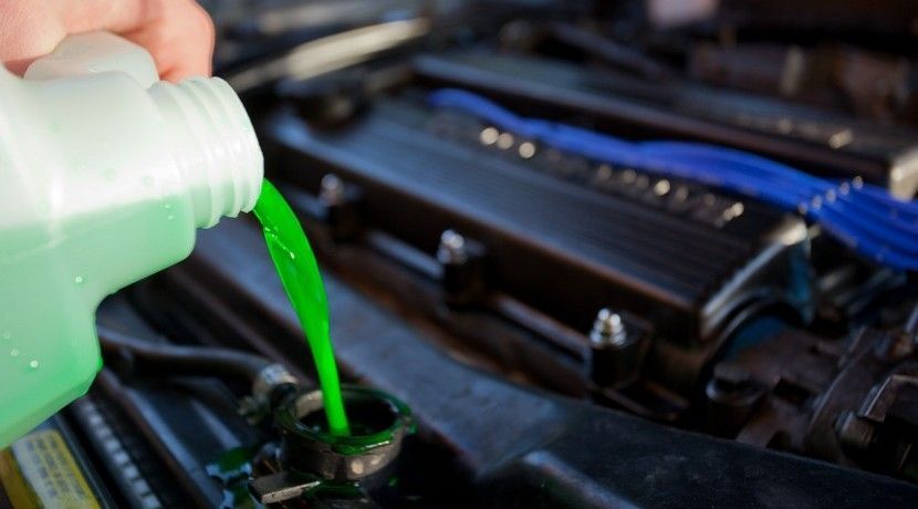 Bright green coolant being poured from a plastic jug into a vehicle's radiator reservoir.