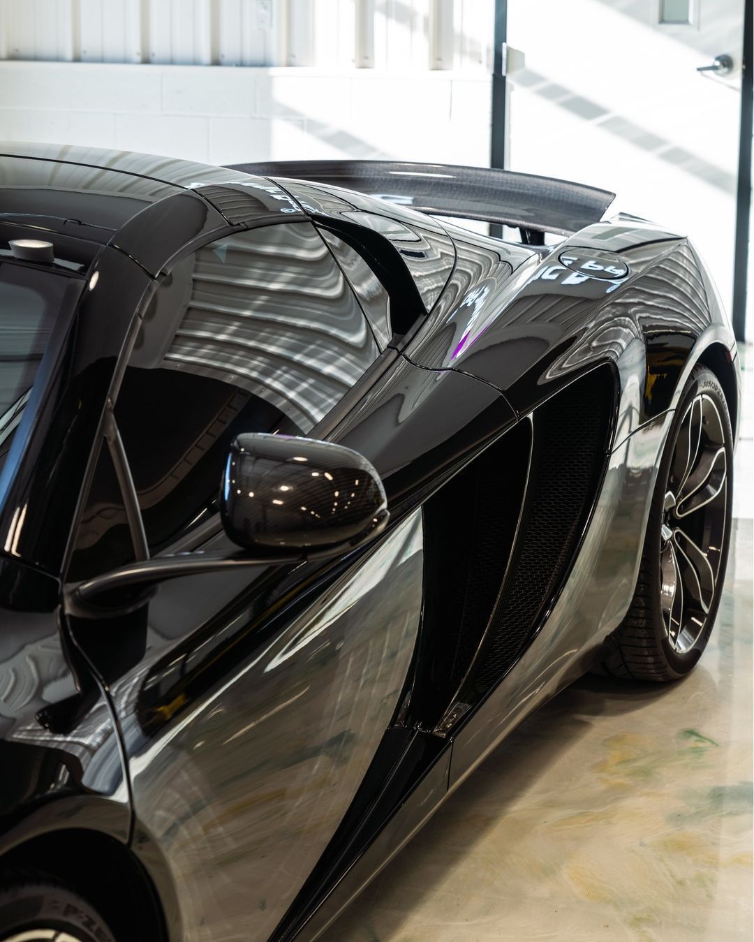 Black sports car displayed indoors, showing its sleek side and rear design.