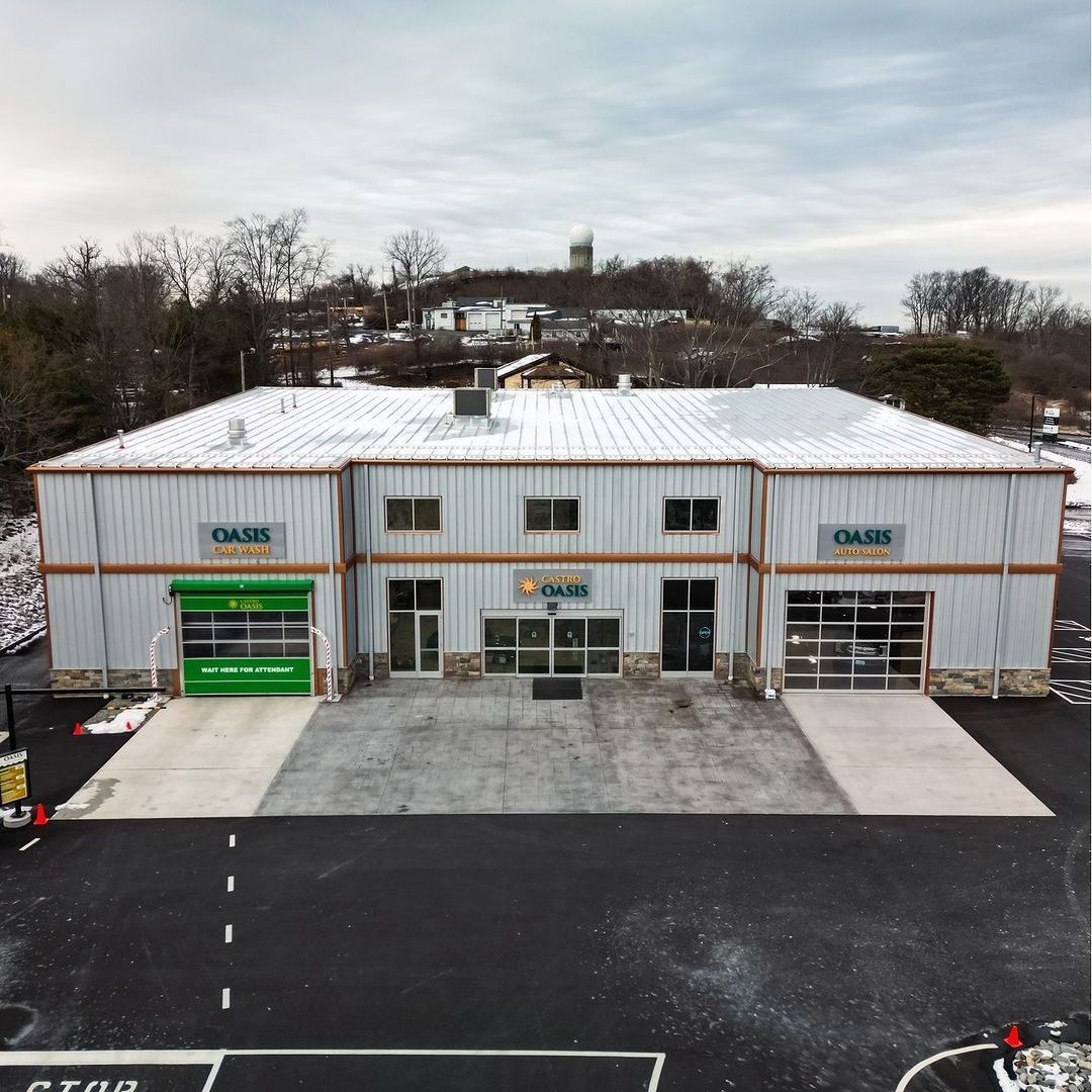 An aerial view of a gray industrial building with three garage-style bays and an Oasis sign, situated in a paved parking lot.