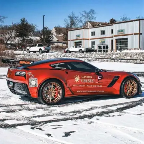 Red sports car with gold rims parked on snow in front of buildings under a clear sky