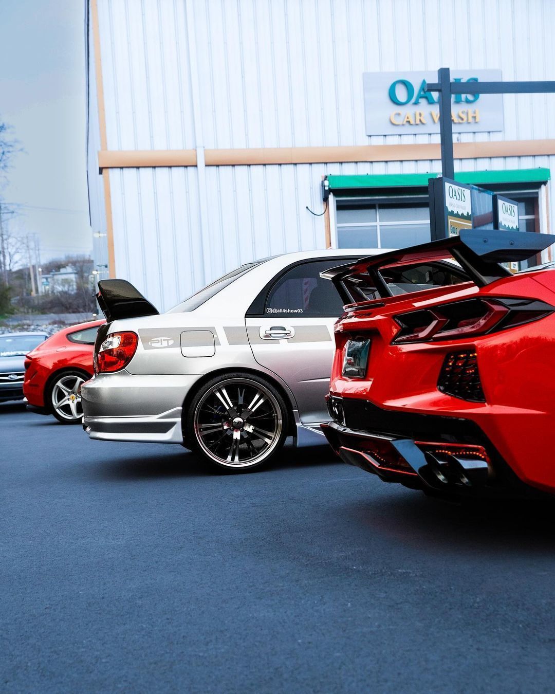 A silver sports sedan and a bright red sports car parked in front of an Oasis Car Wash building.