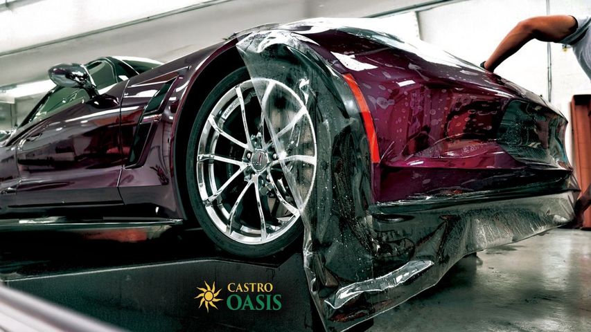 Maroon sports car being hand-washed in a car wash bay, with water and soap splashed on the floor.