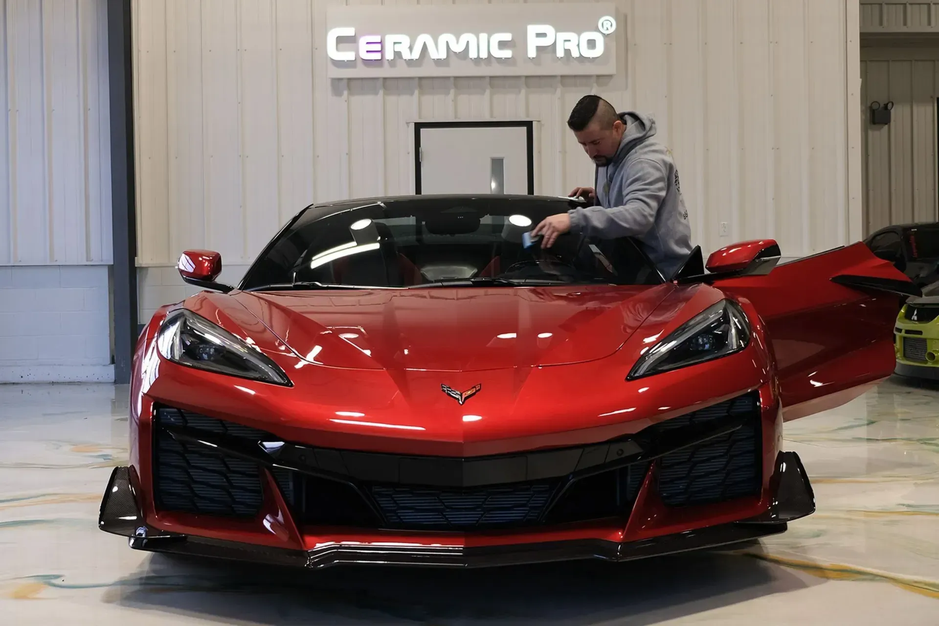 Red sports car being polished by a man inside a ceramic coating shop