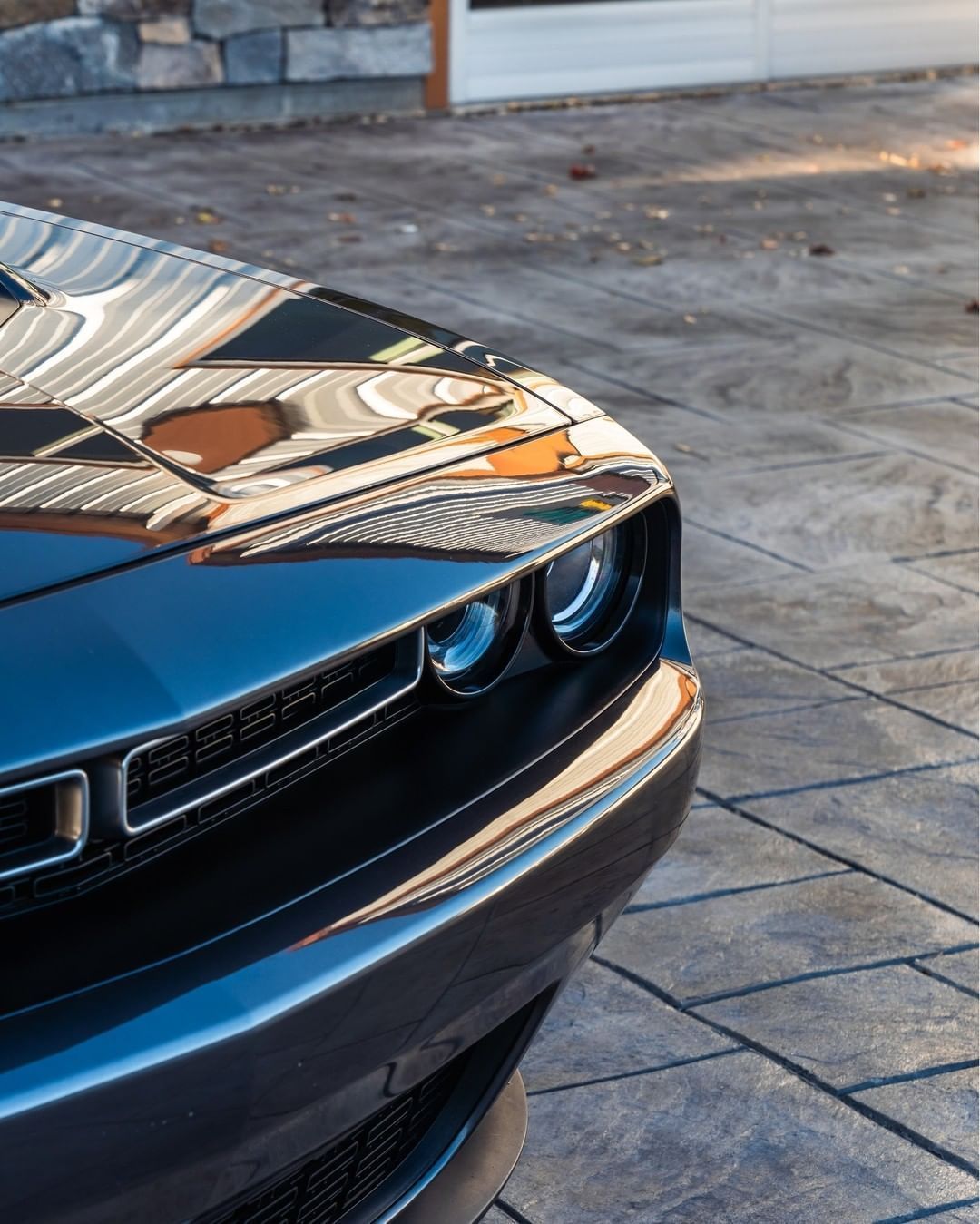 Close-up of the front corner of a dark blue Dodge Challenger parked on a patterned stone driveway.
