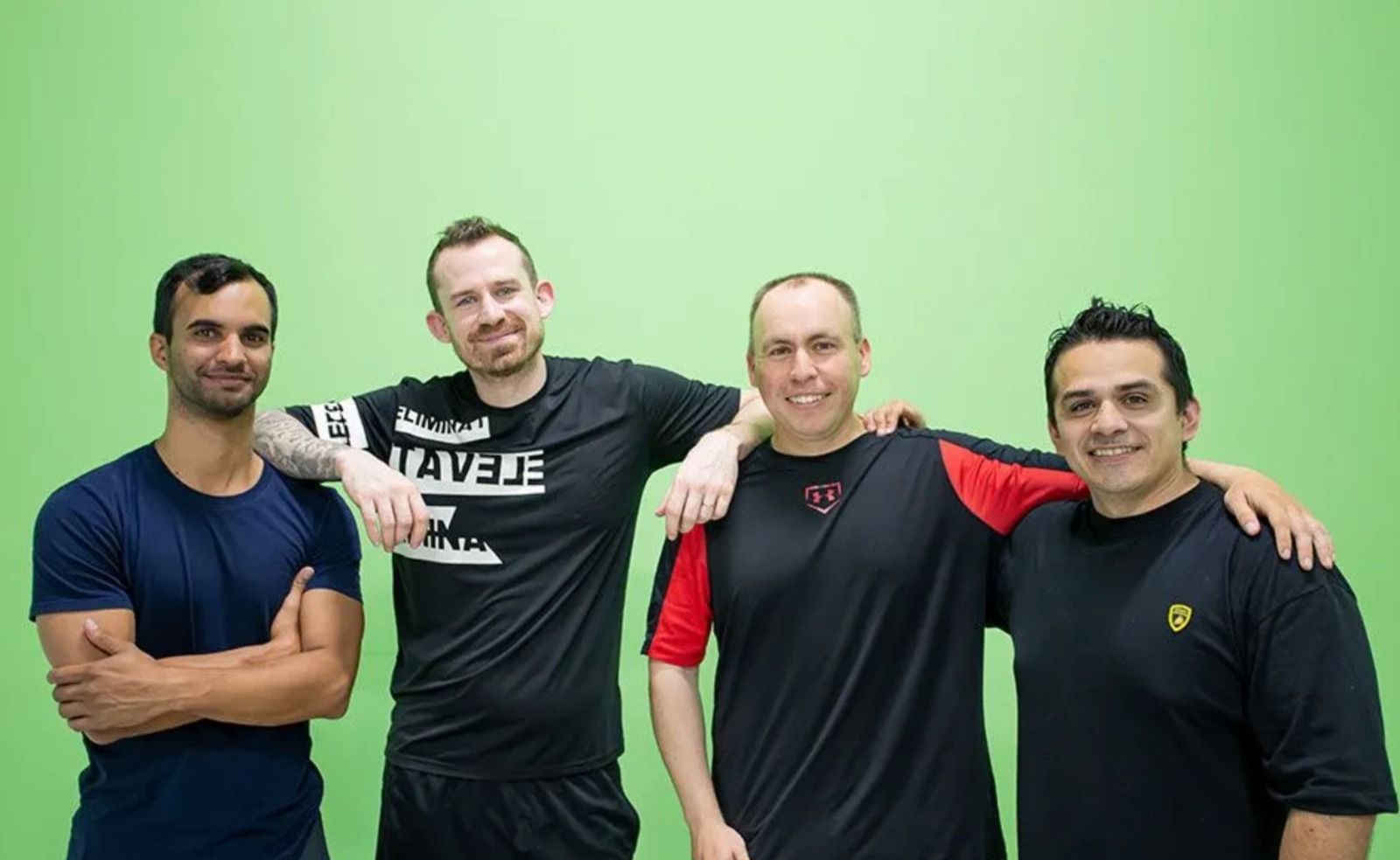 Four men posing together and smiling in front of a bright green background.