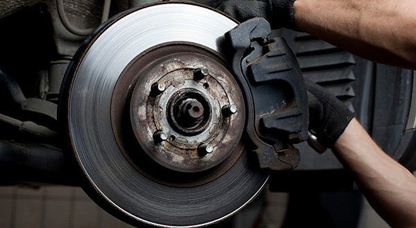 A mechanic wearing gloves works on a car's brake disc and caliper assembly.
