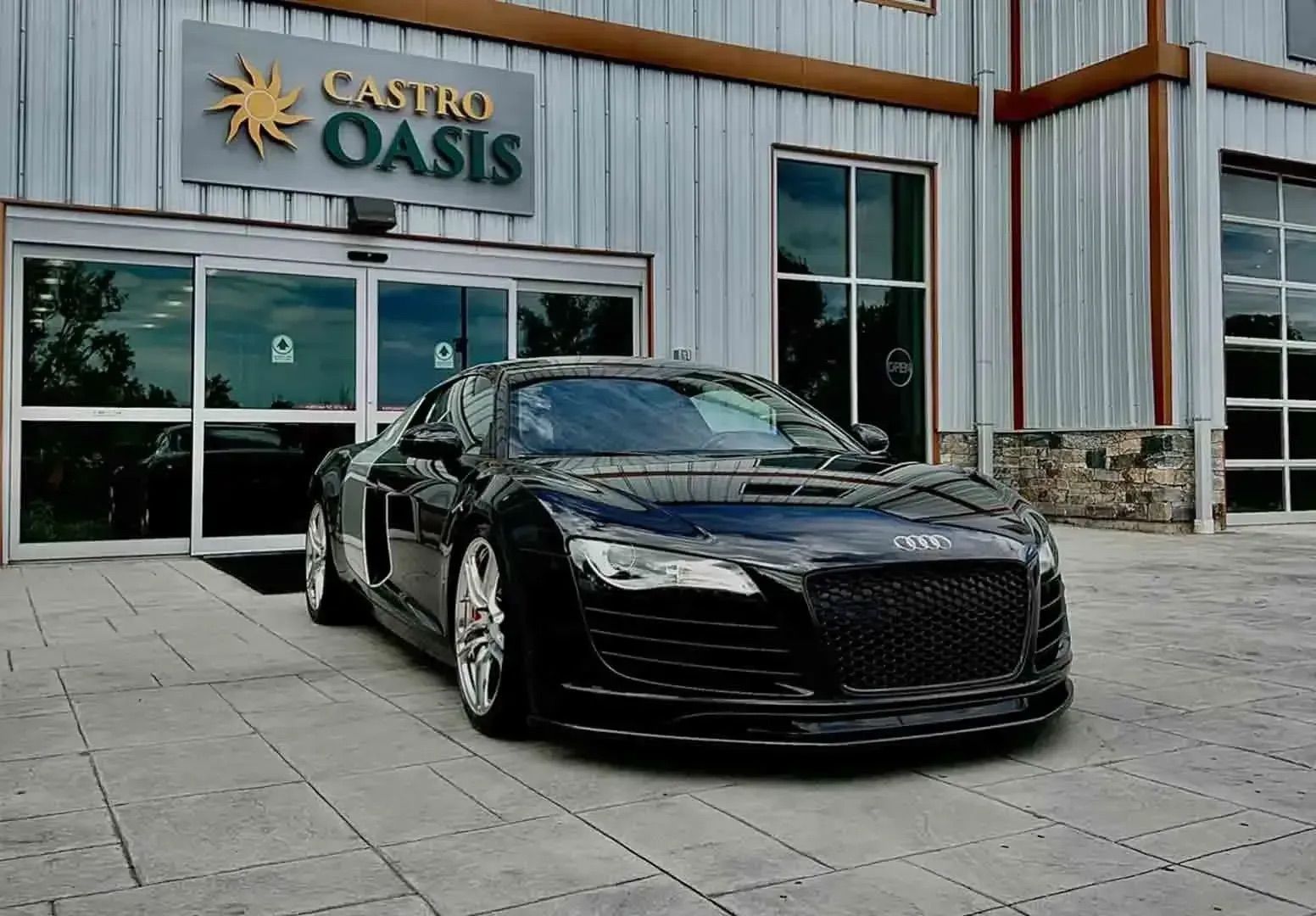 A sleek, black Audi R8 parked in front of a building with a sign that reads 