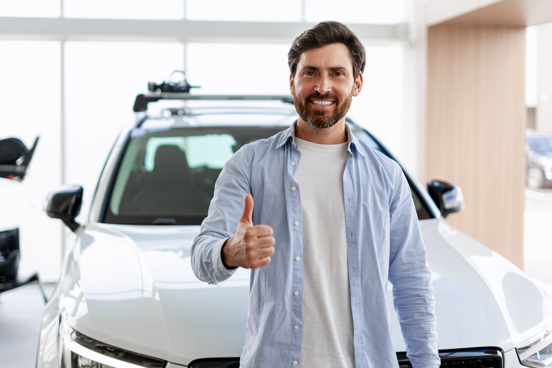 Smiling man giving a thumbs-up in a car showroom beside a white SUV