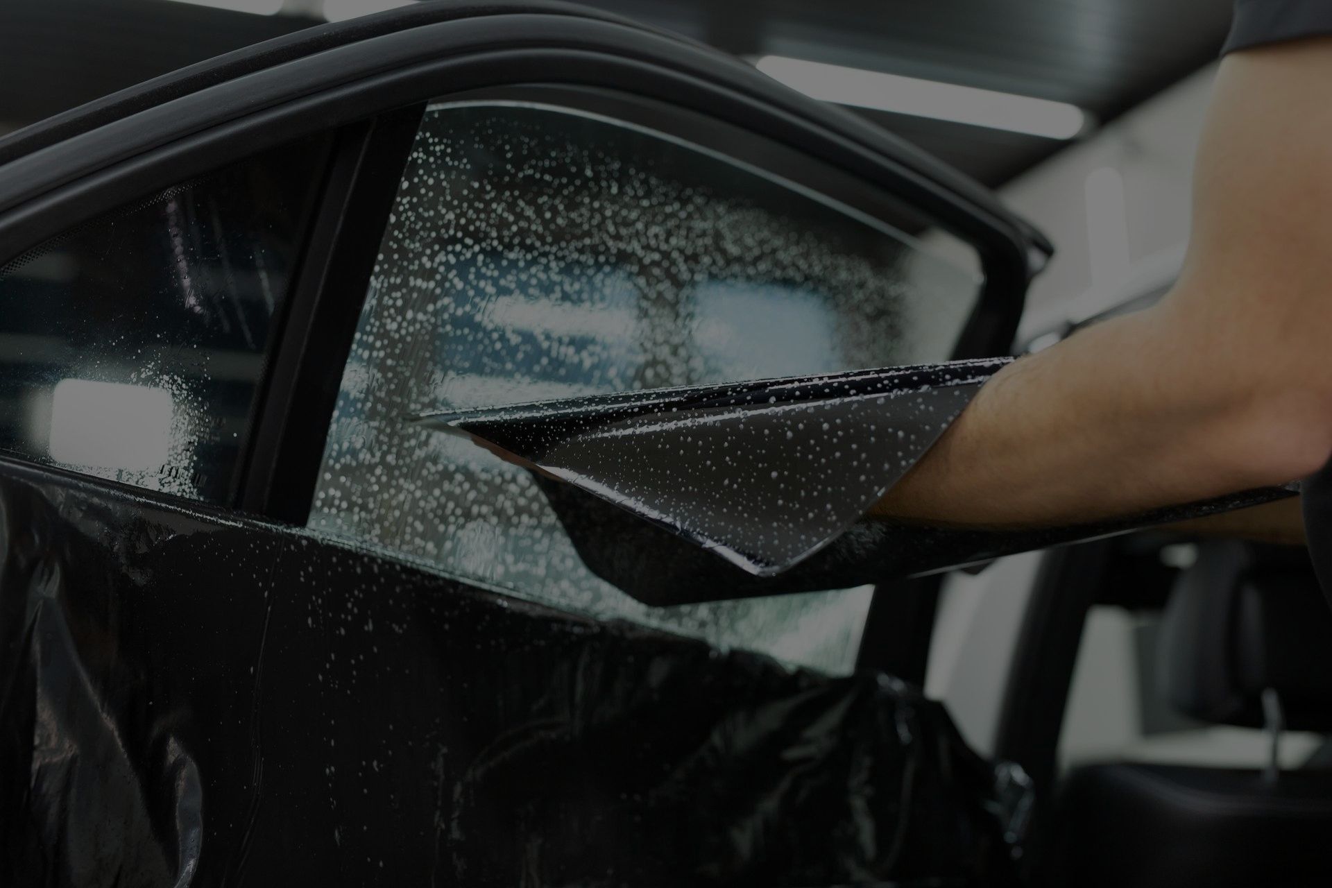 A technician applies dark automotive window tint film to a car window using a squeegee.