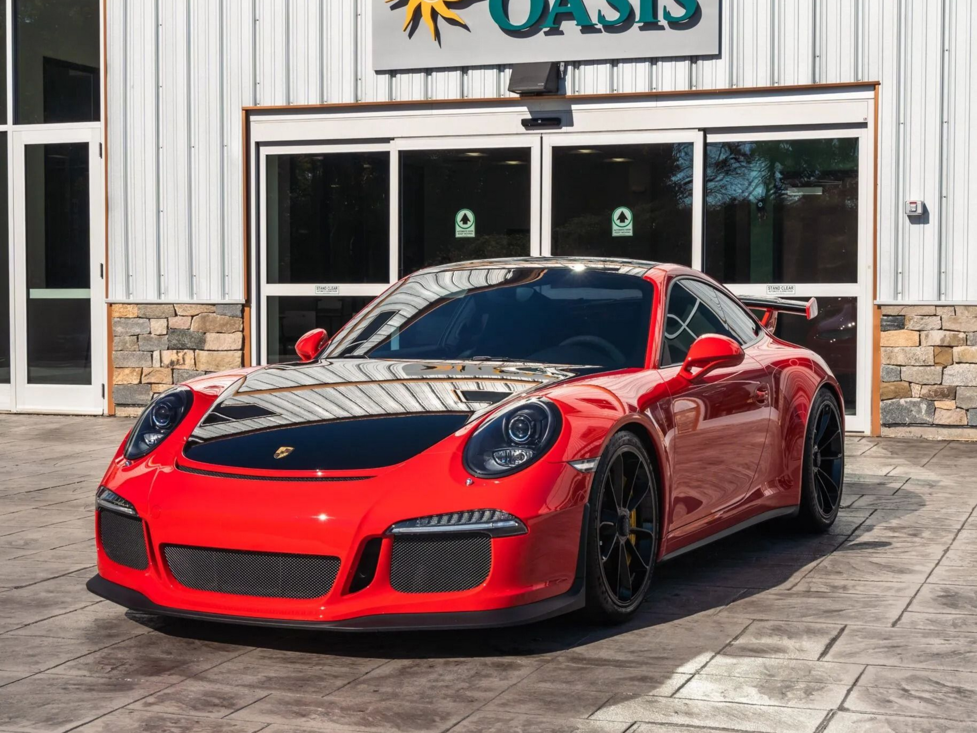 A bright red Porsche 911 GT3 with black wheels and a black hood parked in front of a building entrance.