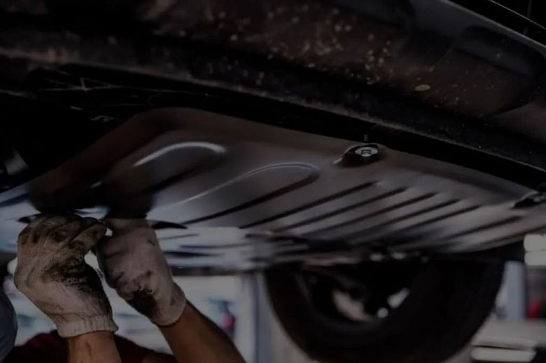 A mechanic in work gloves performs maintenance on the underside of a vehicle lifted in a garage.