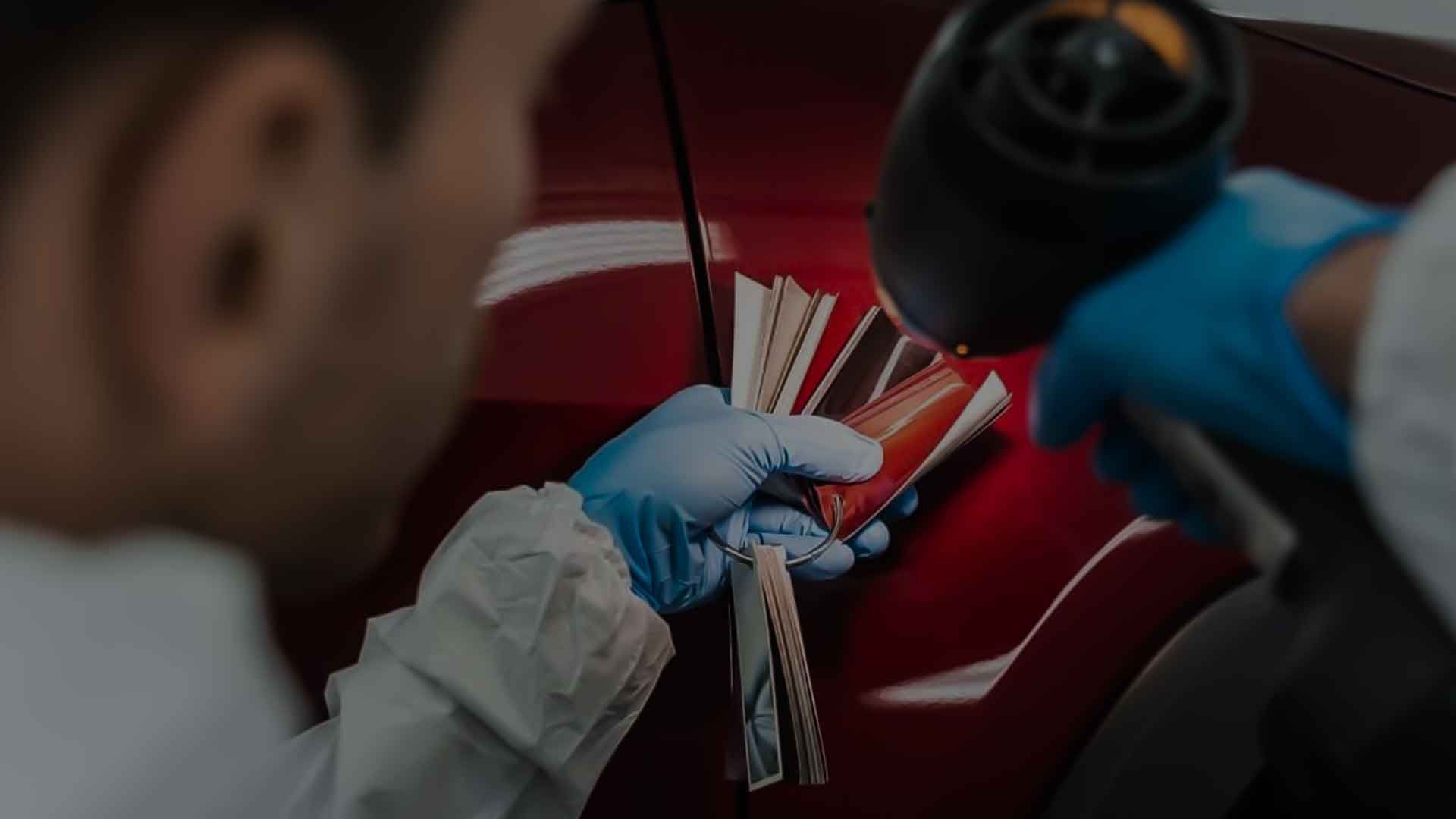 A person wearing blue gloves uses a heat gun to apply red automotive vinyl film to a vehicle panel.