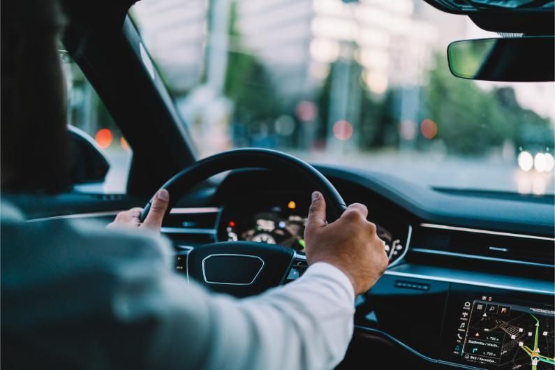 Driver holding the wheel in a modern car, driving through a city at dusk