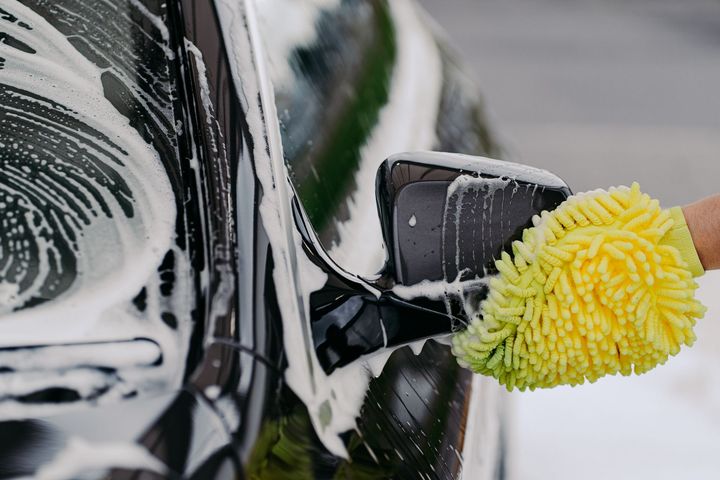 Yellow sponge washing a black car mirror covered in soap foam